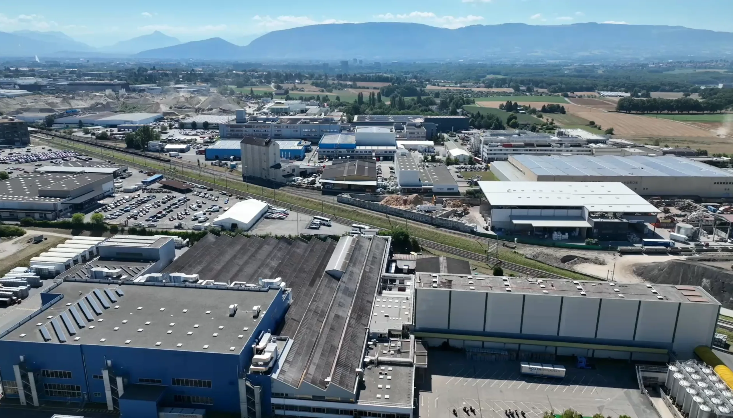Vue aérienne de la zone ZIMOGA, grandes halles et silos, montagnes à l'horizon