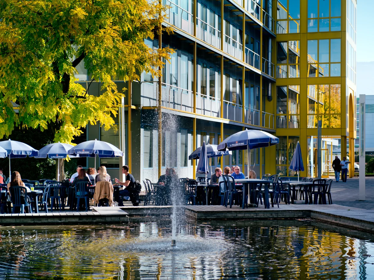 Terrasse d'un café avec parasols et bassin, au pied d'un bâtiment moderne en zone d'activités