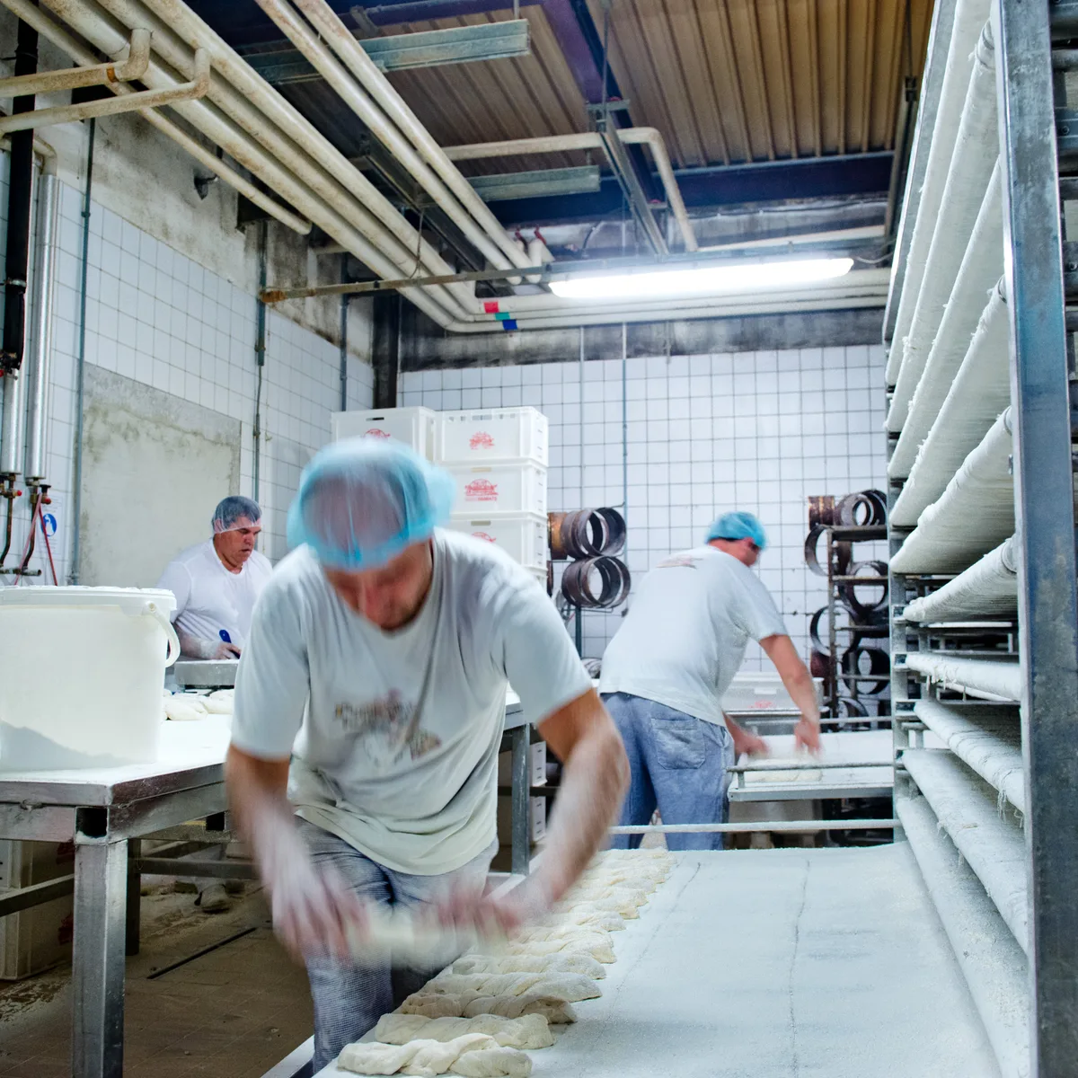 Fournil de boulangerie : boulangers façonnant des pâtons de pain sur un plan de travail fariné